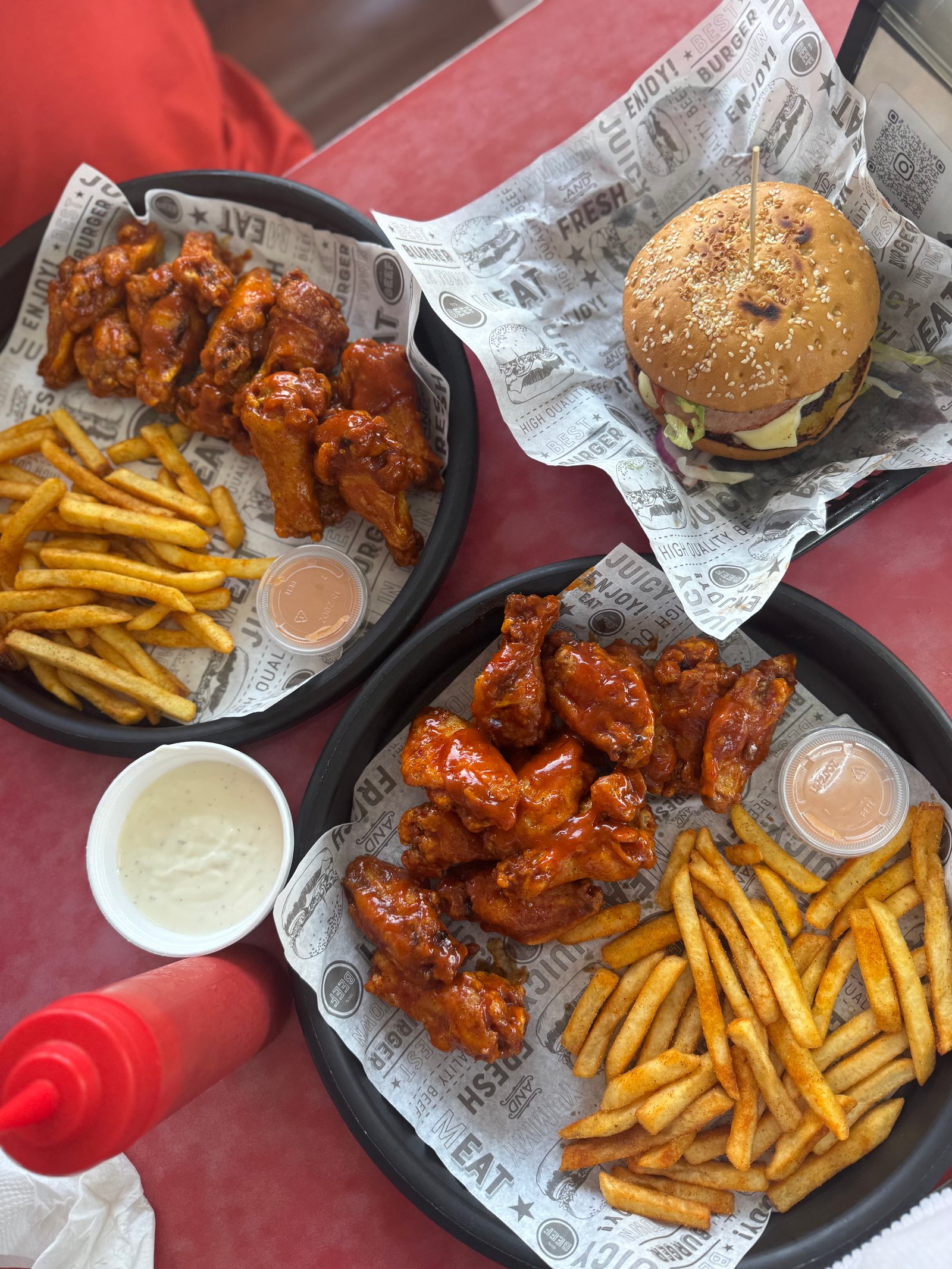 Two baskets of sauced chicken wings with seasoned fries and a sesame bun burger on a red table